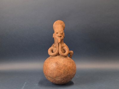 une vieille figurine en argile représentant une femme assise sur une boule