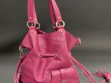 the pink purse is sitting on a gray surface with a tassel around it
