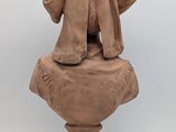 statue of a woman sitting on a stone bust with a hat on