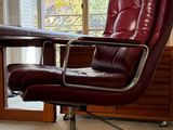 a red leather office chair sitting in front of a window