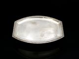 an antique silver plate with a decorative edge on a black surface