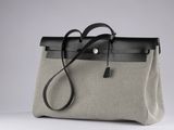 a grey and black bag with a black handle on a white surface