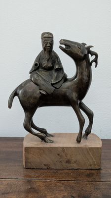 a statue of a man riding a camel on a wooden block