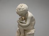 a white statue of a boy sitting on a rock