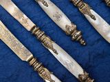 six antique silverplated knives on a blue cloth with a blue background