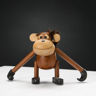 singe en bois tenant une paire de ciseaux sur une surface blanche