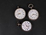 trois montres de poche anciennes posées sur une surface noire, avec des chiffres romains
