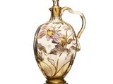 une image représentant un vase en verre muni d'une anse dorée, posé sur une surface blanche