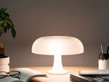 La lampe est posée sur une table, à côté d'un livre et d'une plante.