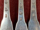 three silver spoons with monograms on them sitting on a red cloth