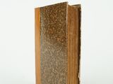 an old book with a brown cover sitting on a white surface