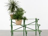 un banc en métal vert sur lequel est posé un panier contenant une plante