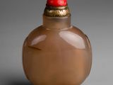 brown glass snuff bottle with a red lid on a gray surface
