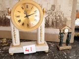 une horloge en or posée sur une table en marbre, à côté d'une petite figurine