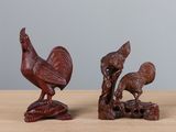 une paire de figurines en bois représentant des coqs, posées sur une table en bois devant un fond gris
