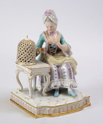 une figurine représentant une femme assise sur une table, avec une cage à oiseaux