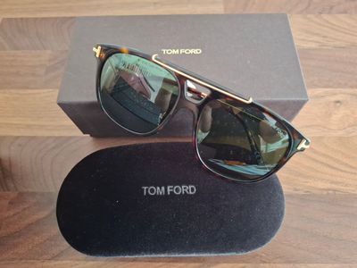 Lunettes de soleil Tom Ford avec leur boîte et leur étui, posées sur une table en bois