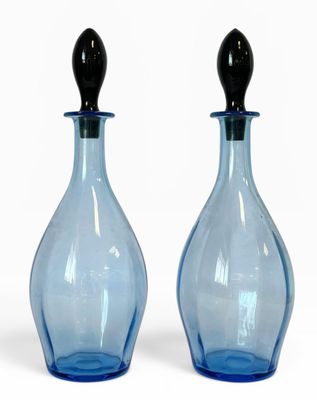 deux bouteilles en verre bleues avec des bouchons noirs, posées sur une surface blanche