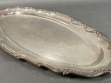 an antique silver plate with a decorative edge on a gray surface