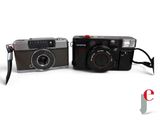 two cameras sitting next to each other on a white surface
