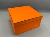 une boîte orange dont le couvercle est ouvert, posée sur une surface blanche