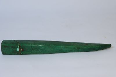 une vieille pipe verte avec un manche en bois, posée sur une surface blanche