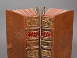 two old books are stacked on top of each other on a gray surface
