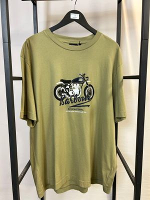 un t-shirt vert orné d'une moto, posé sur un porte-vêtements devant un mur blanc