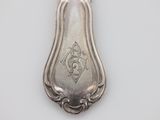 an old silver spoon with a design on it on a white surface