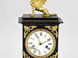 une horloge noire et dorée sur laquelle figure un personnage ailé