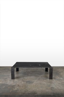 une photo d'une table basse noire posée sur un sol en béton