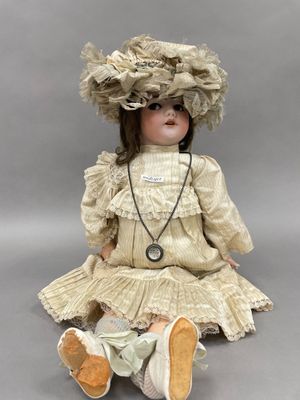 une poupée ancienne assise par terre, vêtue d'une robe et d'un chapeau