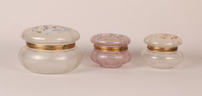 three small glass jars with gold trims and lids on a white surface