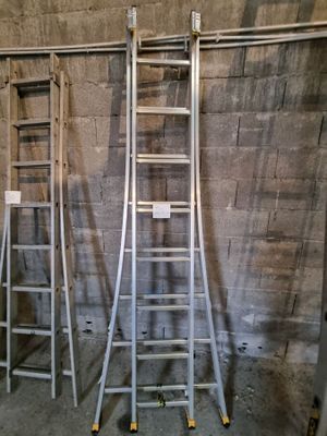Plusieurs échelles sont alignées contre un mur de briques dans une pièce.