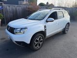 La Dacia blanche est garée devant une clôture en bois.