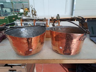 deux grandes casseroles en cuivre posées sur une table, avec un ordinateur portable en arrière-plan