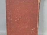 an old red book sitting on top of a table next to a white wall