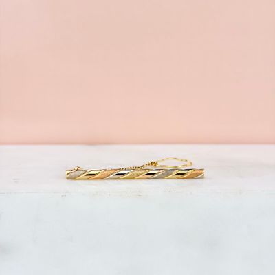 une paire de boucles d'oreilles en anneaux torsadés en or posée sur une table blanche