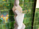 une statue représentant une femme assise sur un bloc devant un mur carrelé de vert