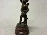 figurine en bronze représentant un garçon tenant un bâton, posée sur un socle en bois
