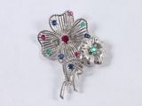 silver flower brooch with multi colored stones on a white background