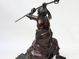 bronze statue of a woman sitting on a rock holding a spear