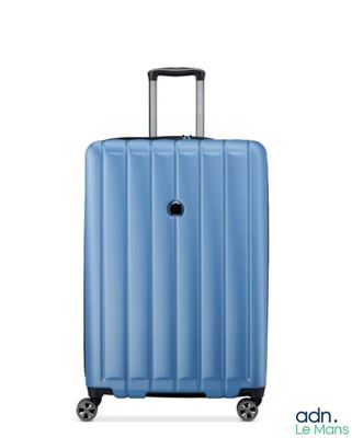La valise bleue repose sur ses roulettes, posée sur une surface blanche.