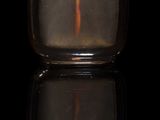 une petite bouteille en verre avec un bouchon rose posée sur une surface noire