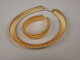 un gros plan d'un collier et d'un bracelet en or posés sur une surface blanche