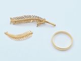 deux bagues en or et une broche en or en forme de plume, posées sur un fond blanc