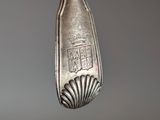 a silver spoon hanging from a hook on a gray wall