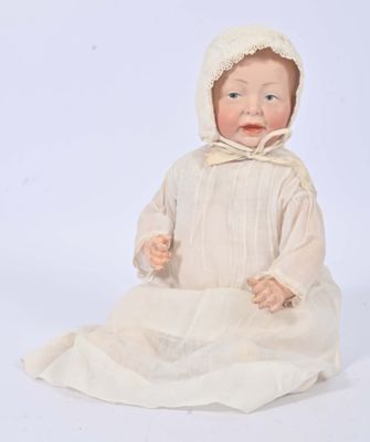 an antique porcelain doll of a baby in a white dress and bonnet