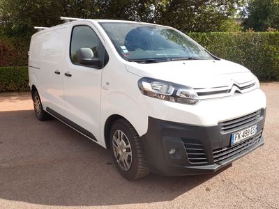 La camionnette blanche est garée sur le parking, près d'une haie.