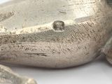 a silver figurine of a frog on a white surface